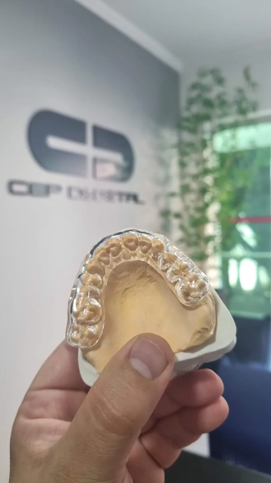 Placa transparente sobre modelo de gesso, com o logo do CEP Digital na parede do laboratório ao fundo